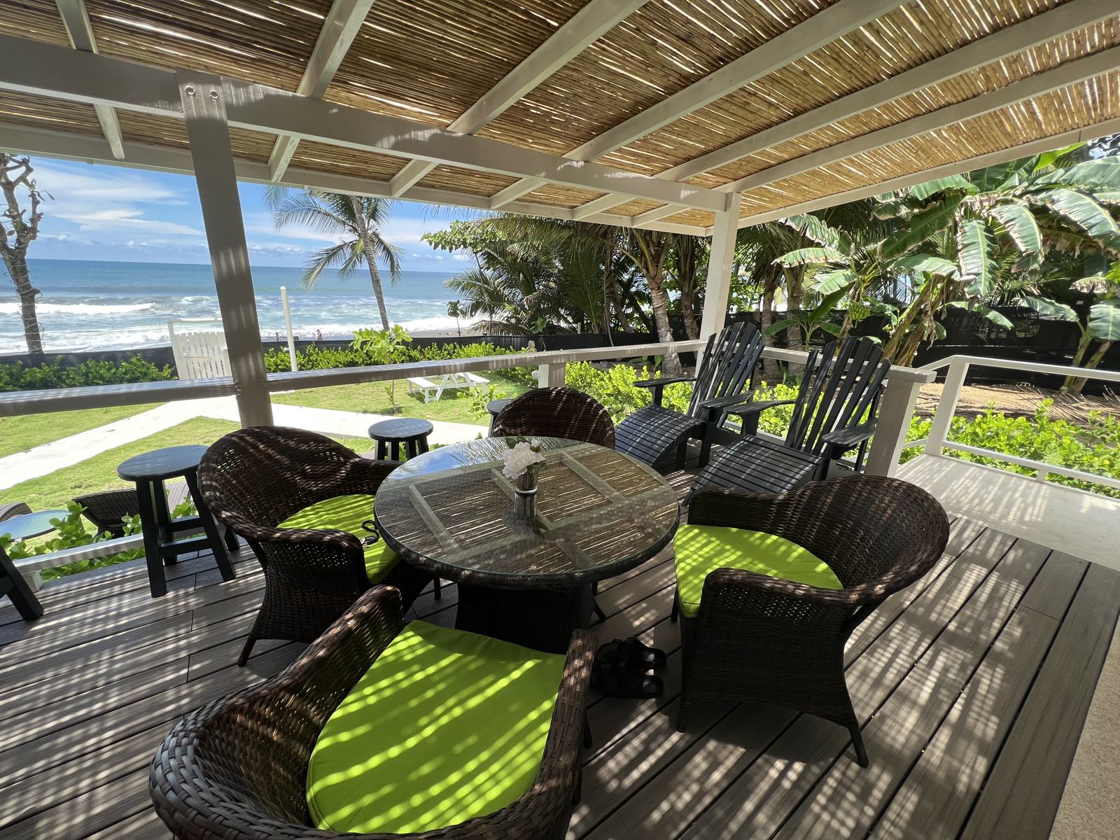 Shaded deck seating under the bamboo roof with the beach and palms beyond