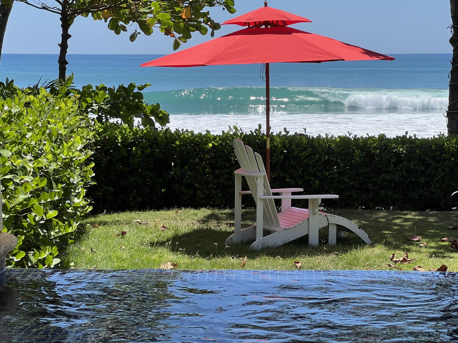 Adirondack chair under a red umbrella on the lawn, with a wave breaking on Playa Hermosa behind